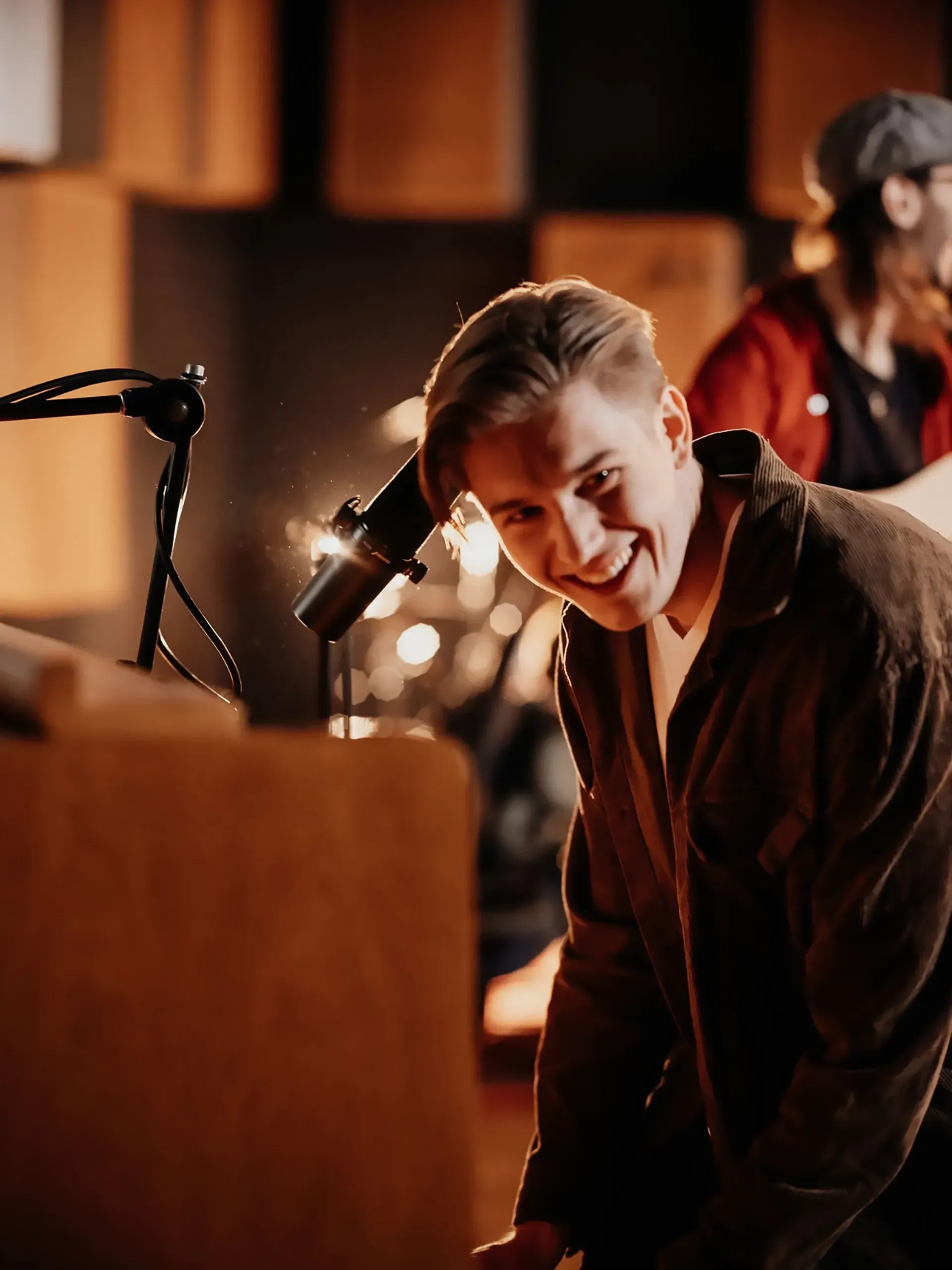 Ein Mann lächelt vor einem Mikrofon in einem Aufnahmestudio.