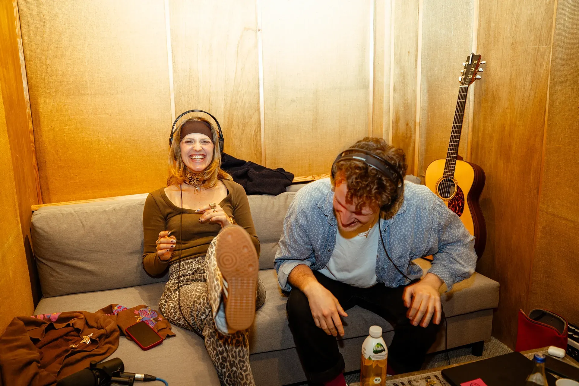 Ein Mann und eine Frau sitzen auf einem Sofa, im Hintergrund steht eine Gitarre.