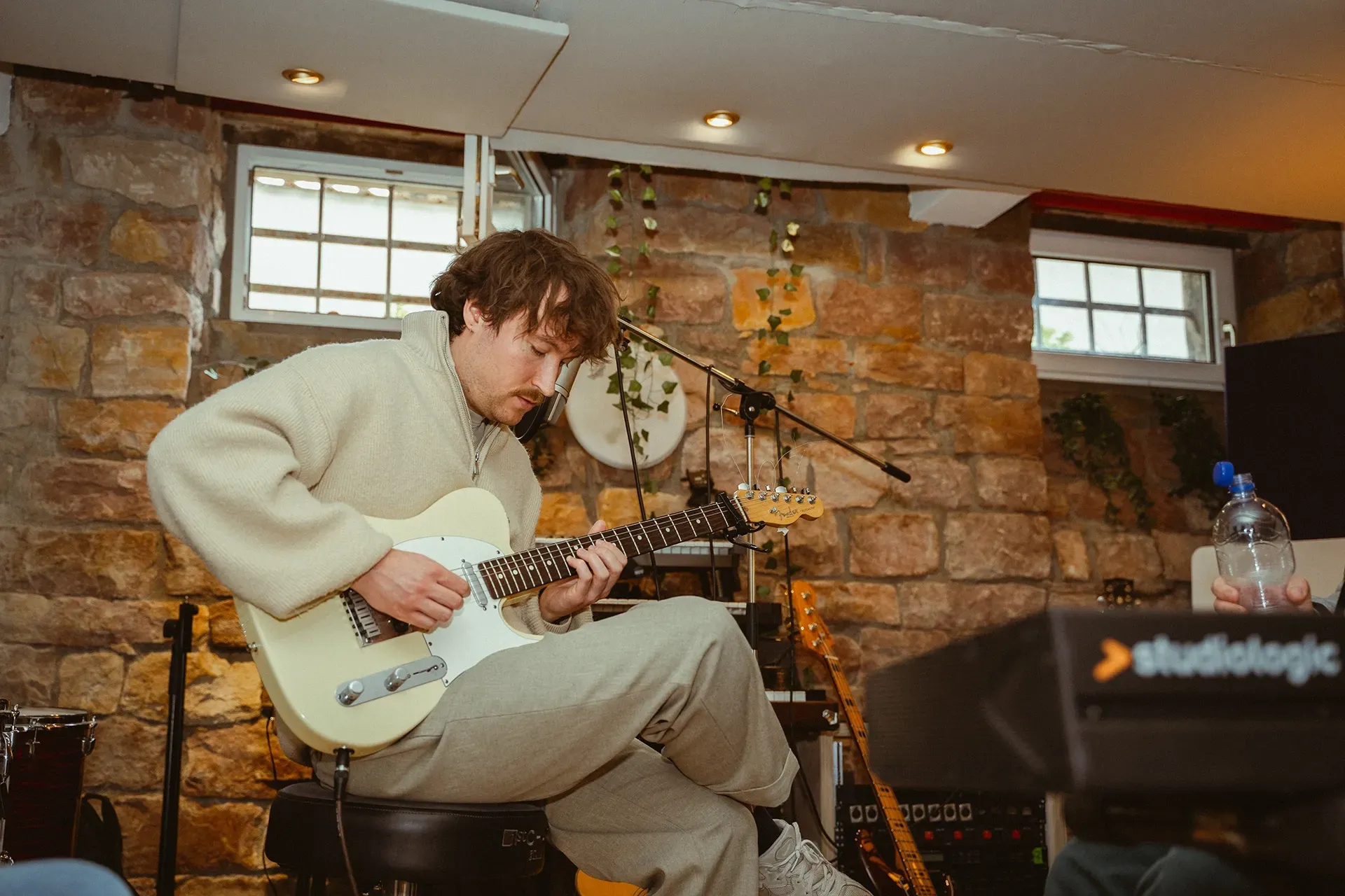 Ein Mann sitzt in einem Raum auf einem Hocker und spielt Gitarre.