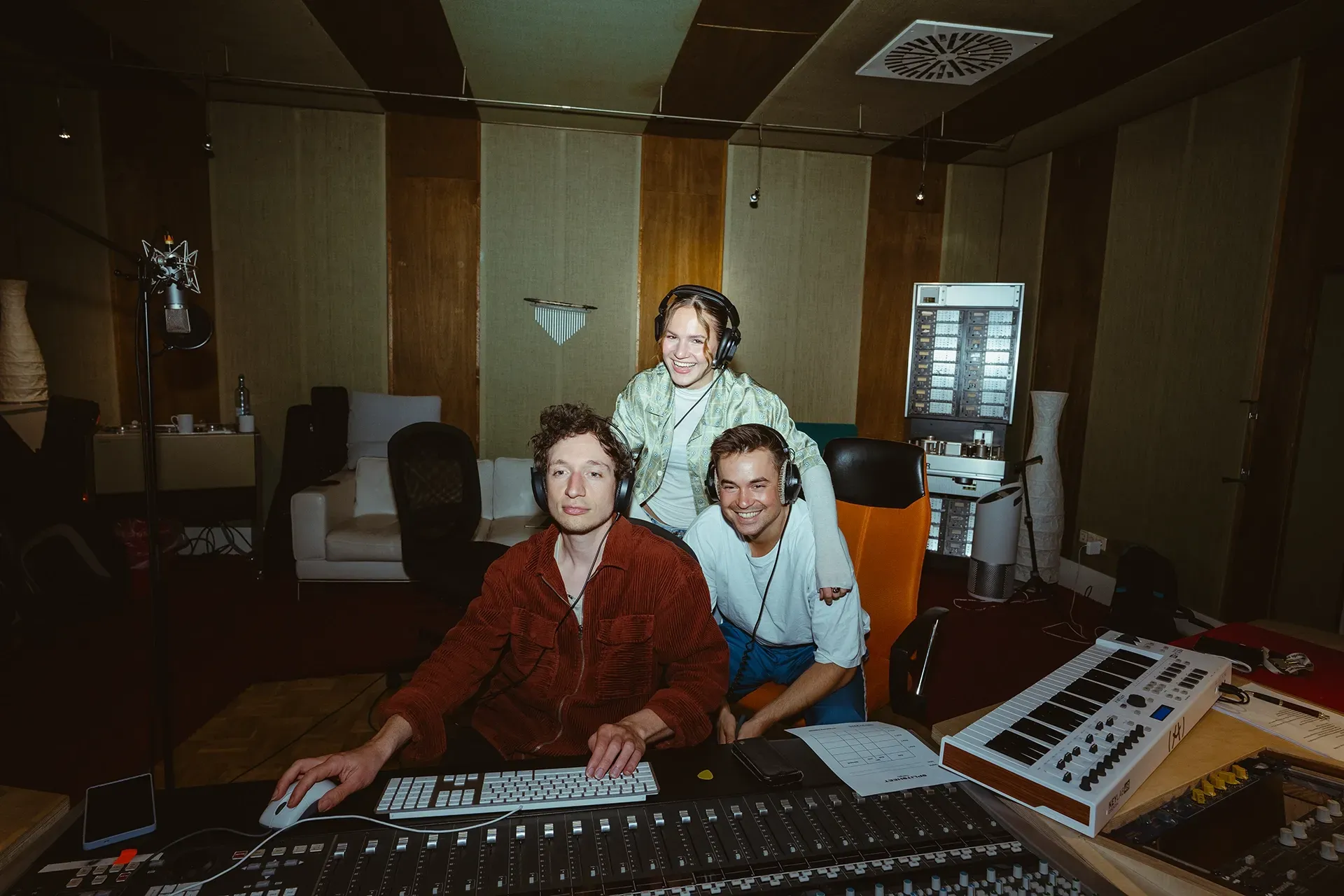 Drei Personen sitzen an einem Mischpult in einem Aufnahmestudio.