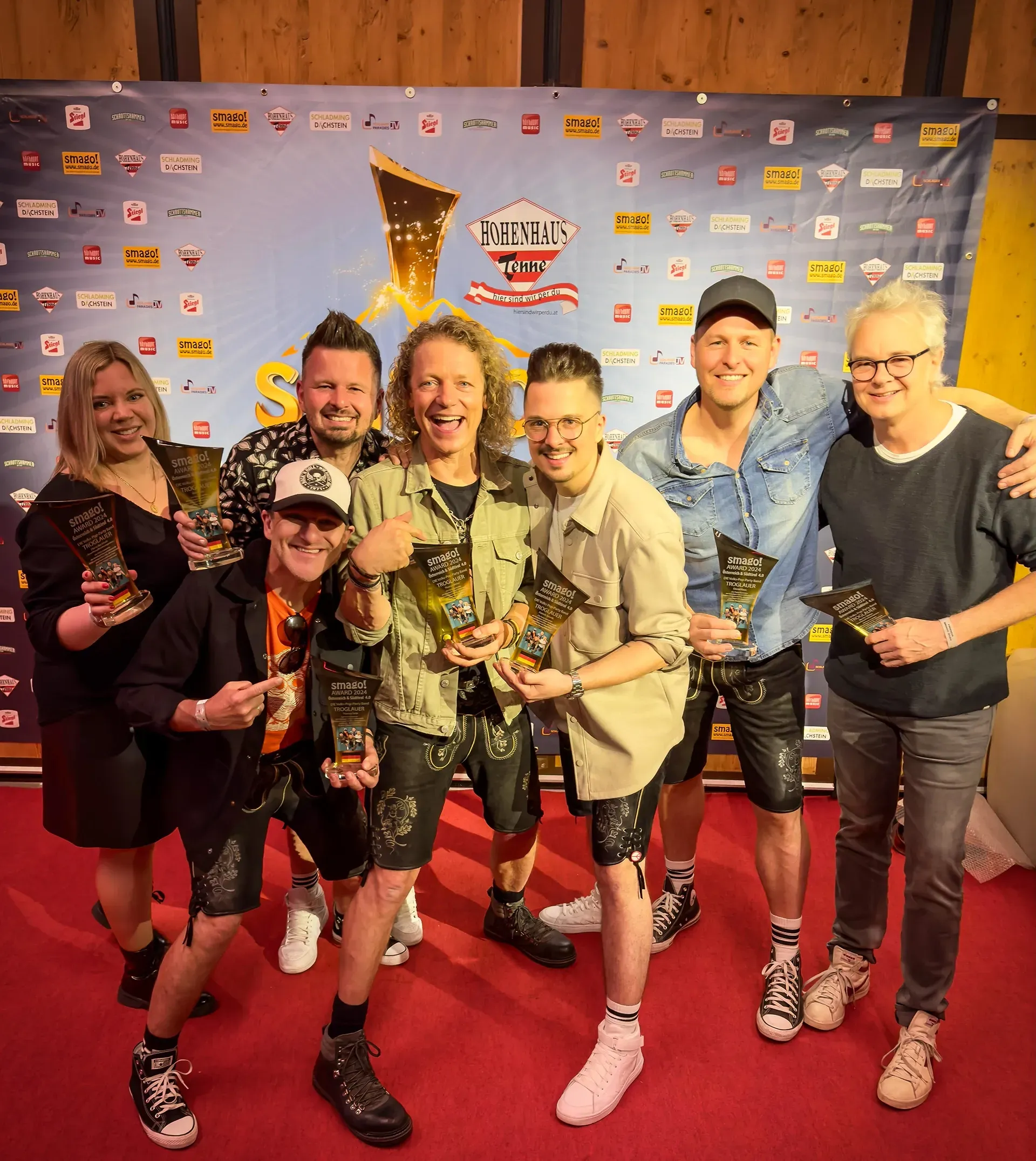 Die Band Troglauer steht auf einem roten Teppich und hält Trophäen in die Kamera