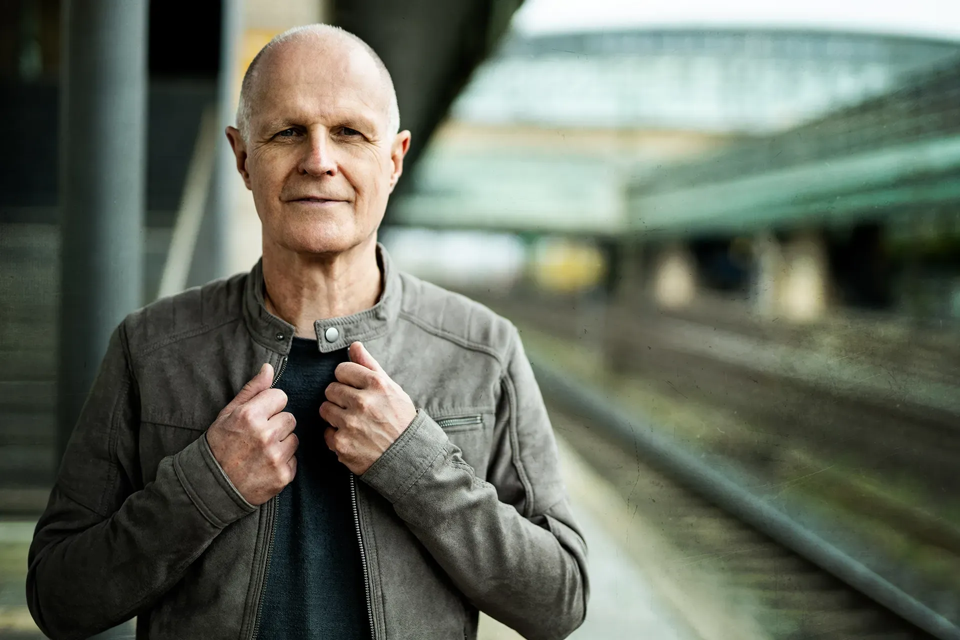 Ein Mann steht mit seiner Jacke in der Hand auf einem Bahnsteig.