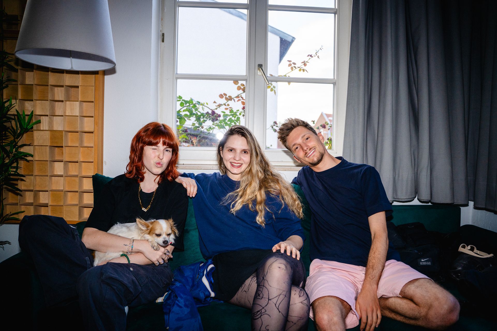 Eine Gruppe junger Künstler sitzen mit einem Hund auf dem Sofa und lachen.