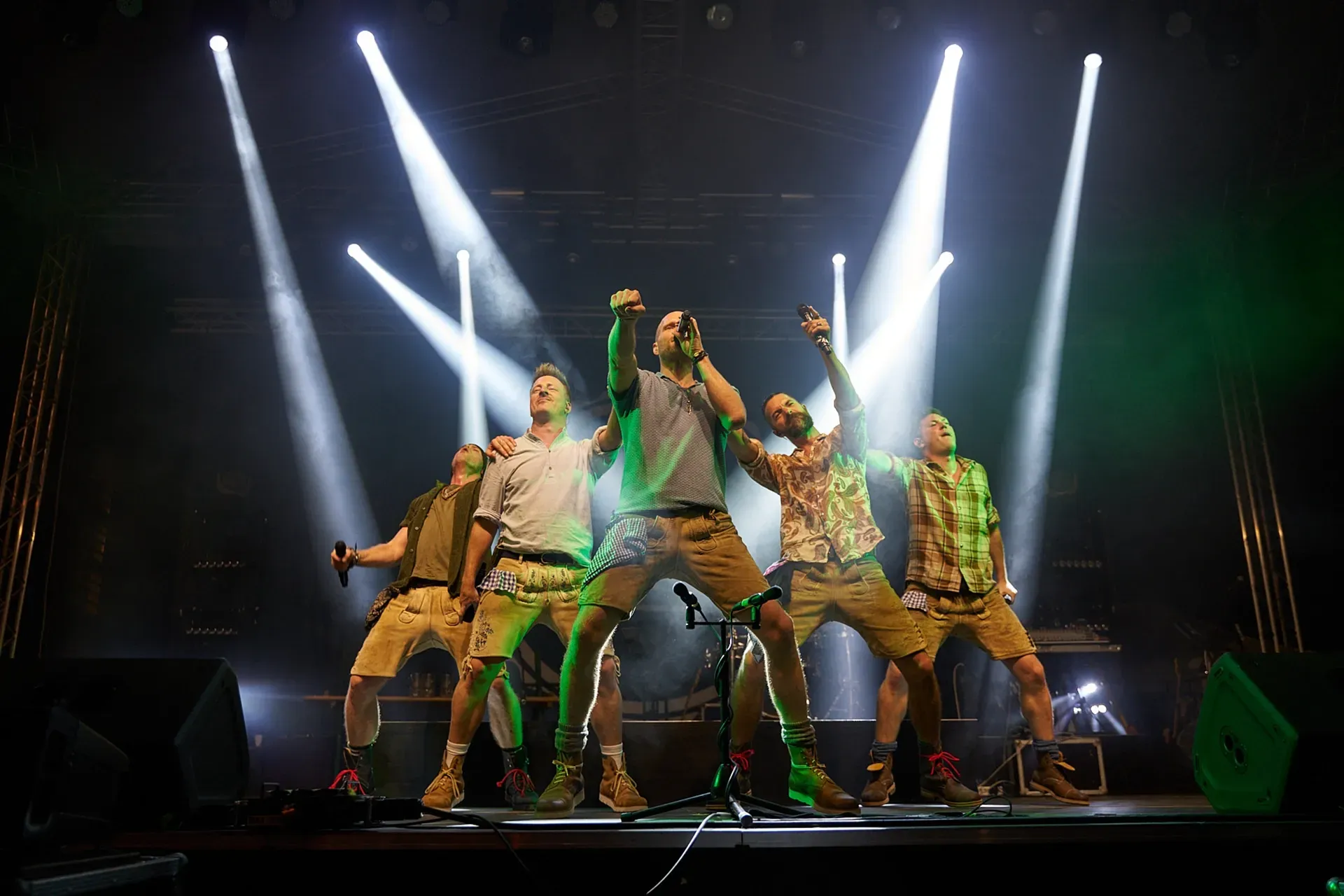 Eine Gruppe von Männern steht mit erhobenen Händen auf einer Bühne.