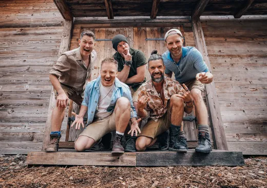 Eine Gruppe Männer posiert vor einem Holzgebäude für ein Foto.
