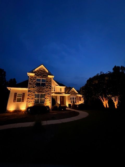 A large house is lit up at night with a blue sky in the background.