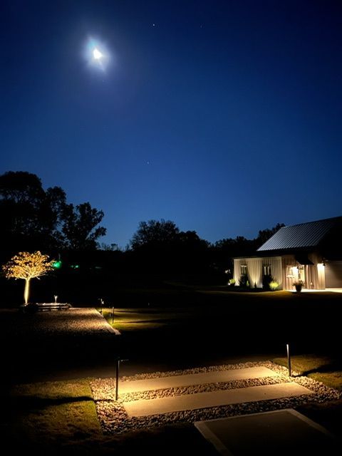 A large house is lit up at night with trees in front of it.