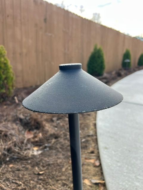 A black light with a cone shaped shade is sitting next to a sidewalk.