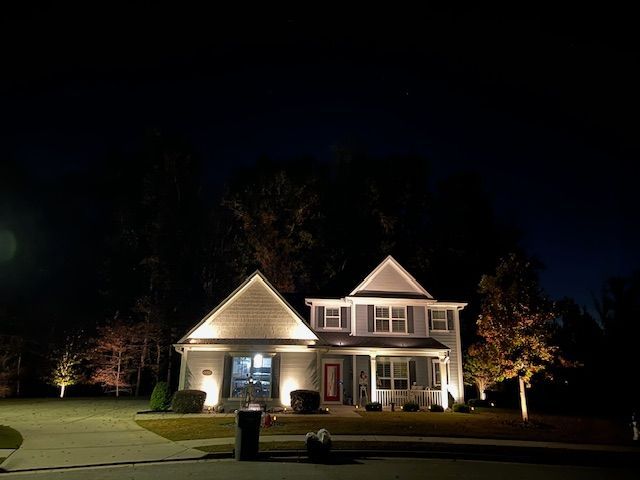A white house is lit up at night with trees in the background.