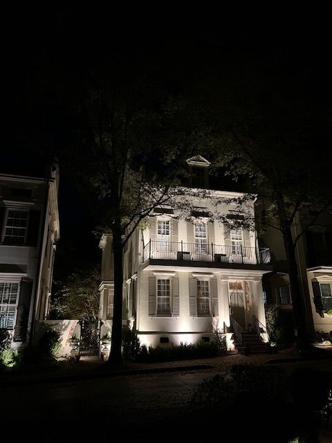 A large white house is lit up at night surrounded by trees.