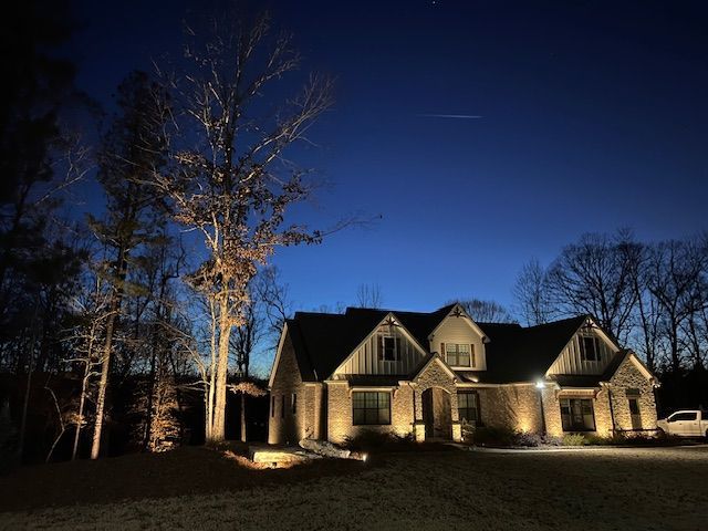 A large house is lit up at night with cars parked in front of it.