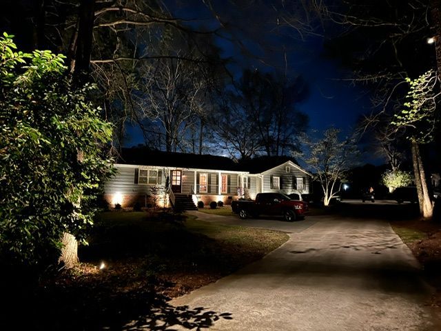 A large house is lit up at night with trees in front of it