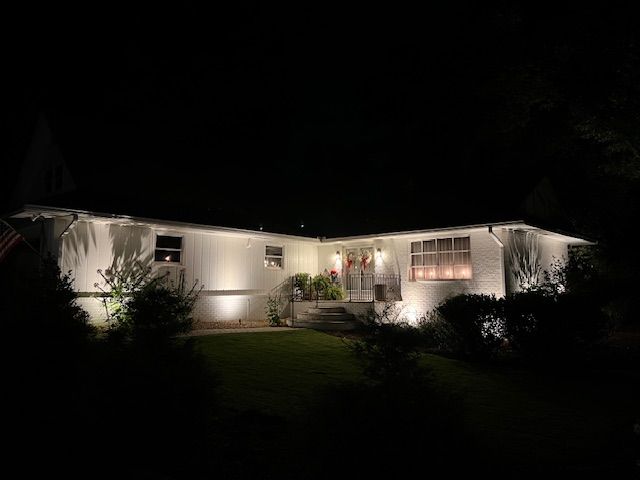 A white house is lit up at night with a brick walkway leading to the front door.
