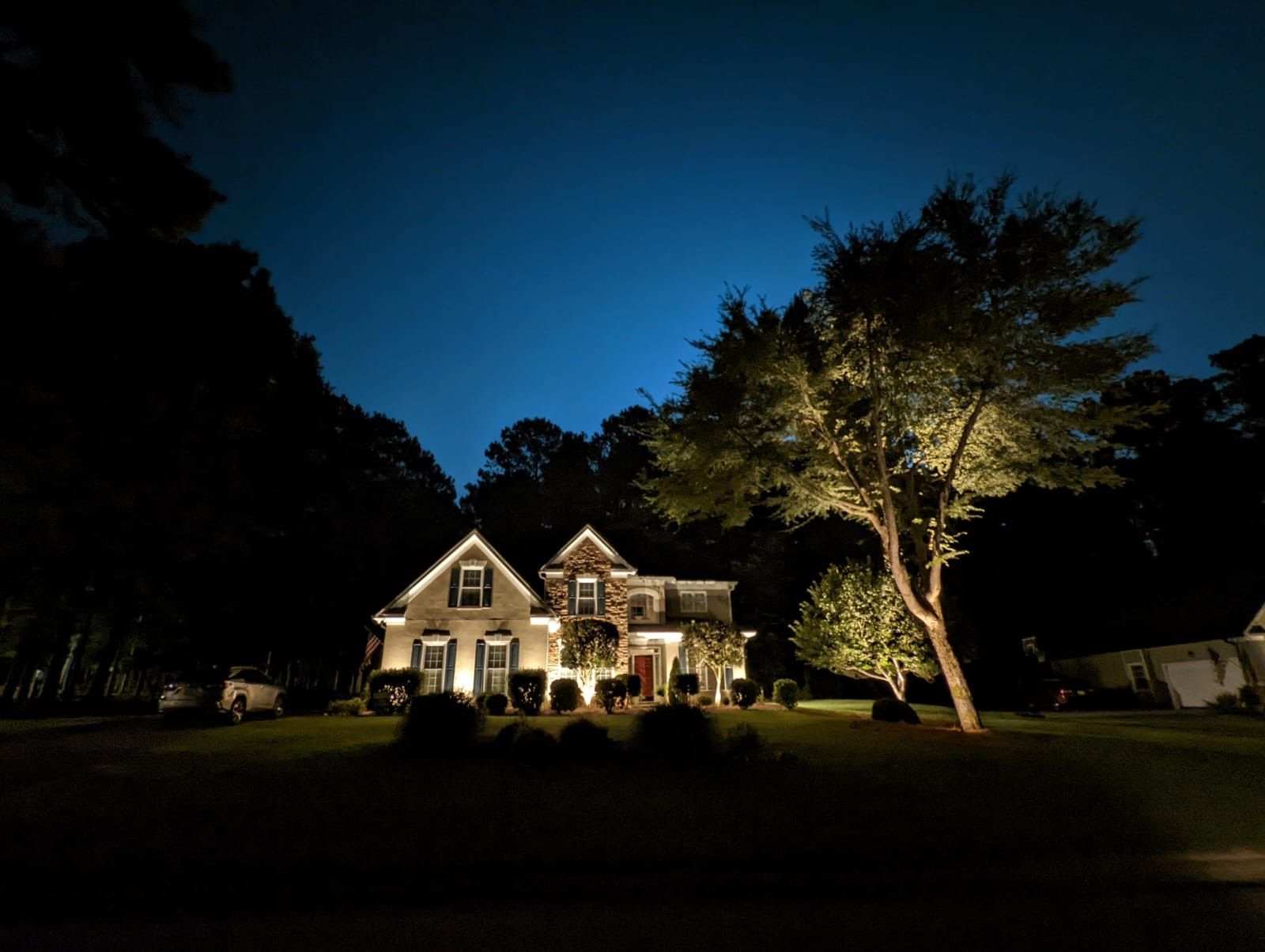 A house is lit up at night with trees in front of it.