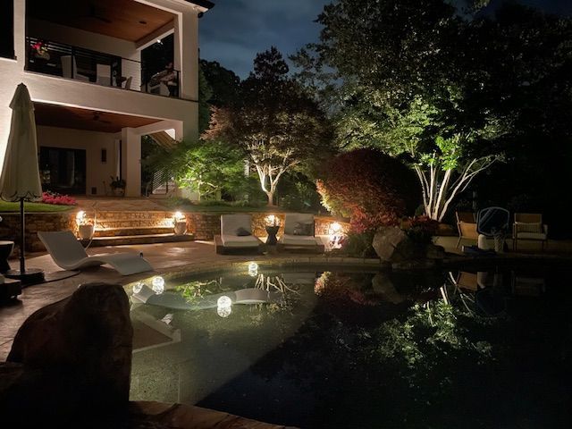 A large swimming pool is lit up at night in front of a house.