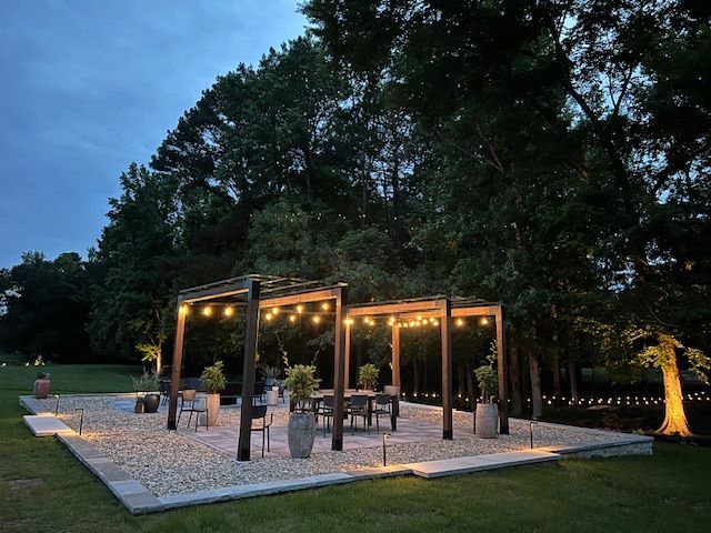 A pergola with a table and chairs underneath it is lit up at night.