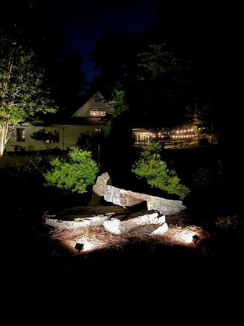 A large rock is lit up at night in front of a house.