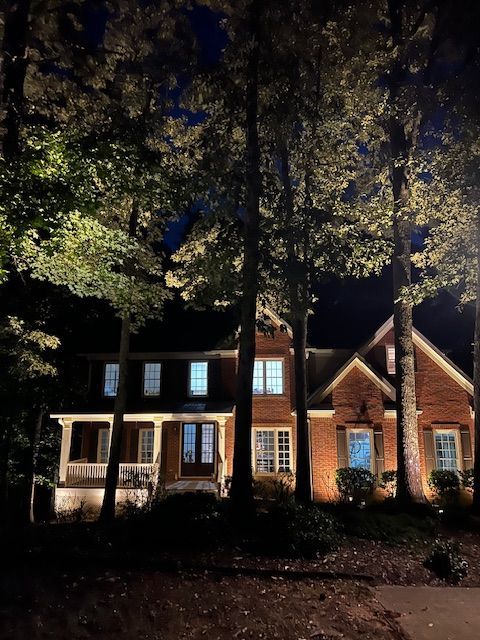 A brick house is lit up at night with trees in front of it.