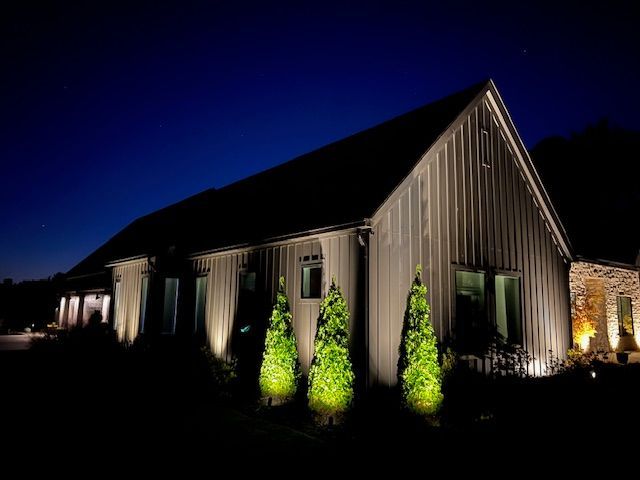 A large house is lit up at night with trees in front of it.