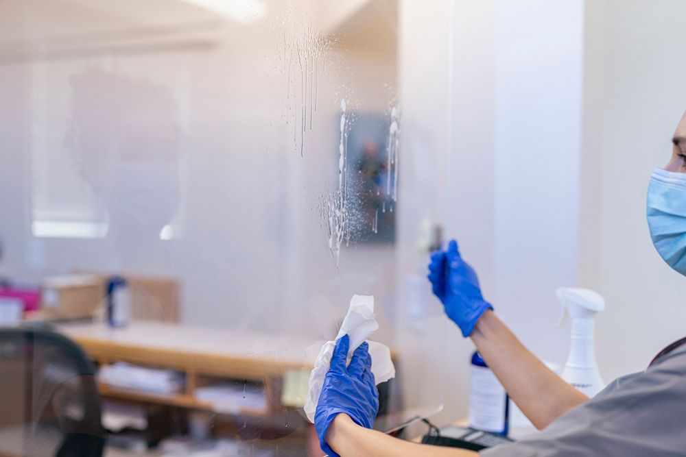 A person wearing a mask and gloves is cleaning a window.