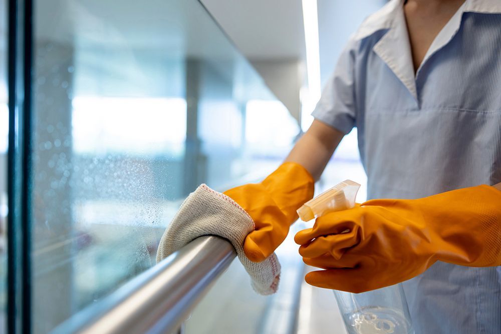 A person wearing orange gloves is cleaning a railing with a cloth.