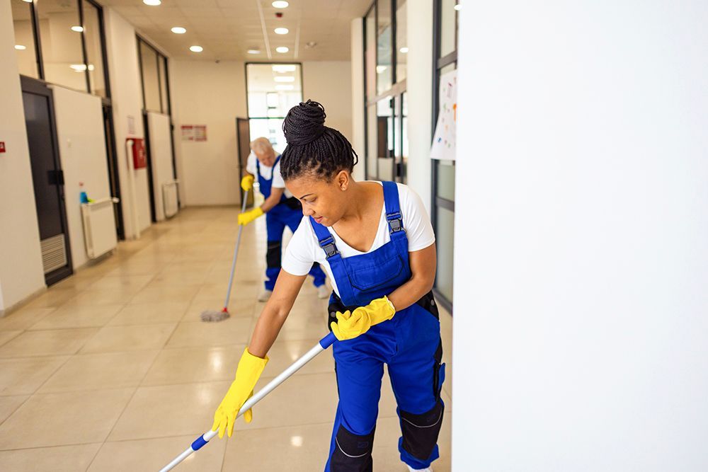 A woman is mopping the floor in a hallway with a mop.