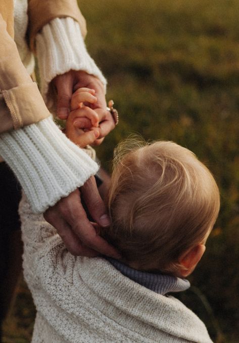 A person is holding a baby 's hand in a field.