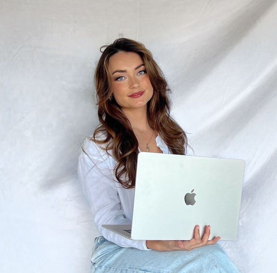 A woman is sitting on a stool holding an apple laptop