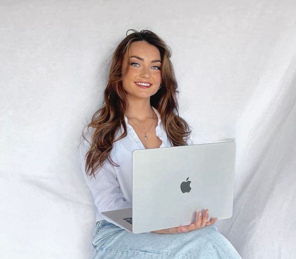 A life insurance agent is sitting on a stool holding a laptop computer.
