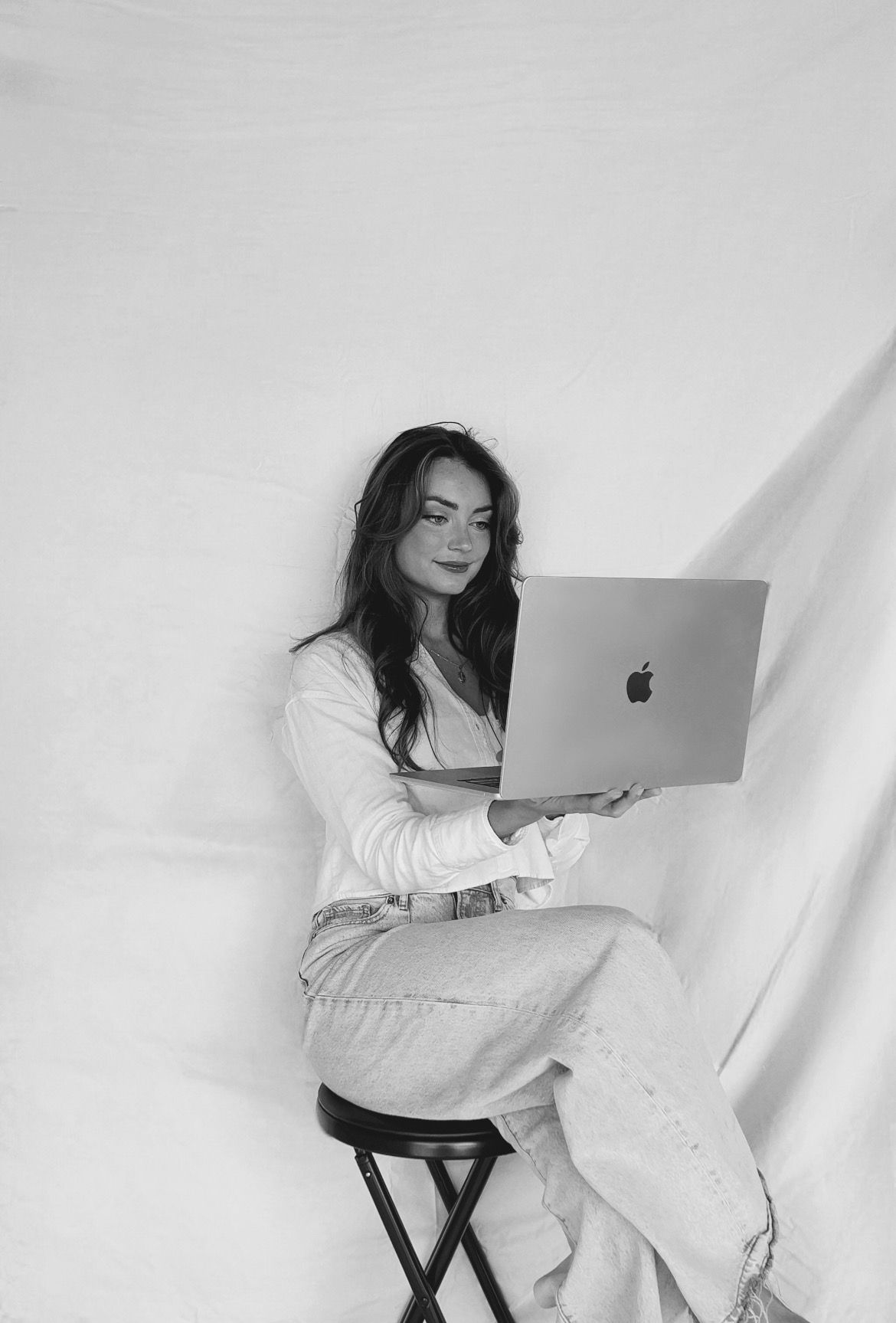 A woman is sitting on a stool holding a laptop computer.