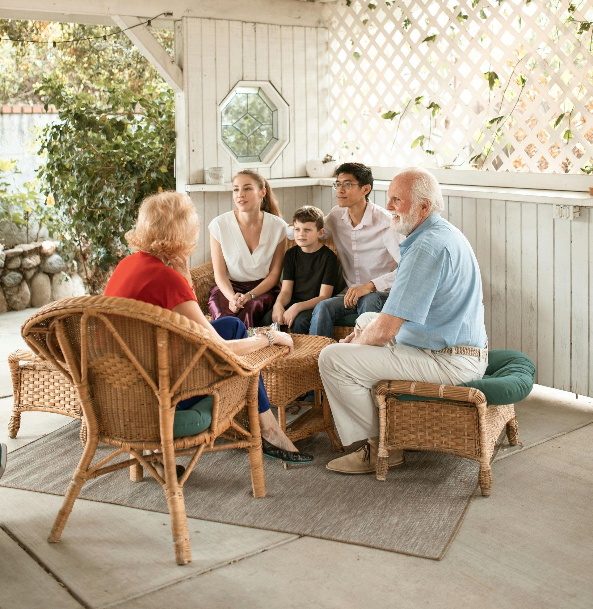 A group of people are sitting in wicker chairs on a porch