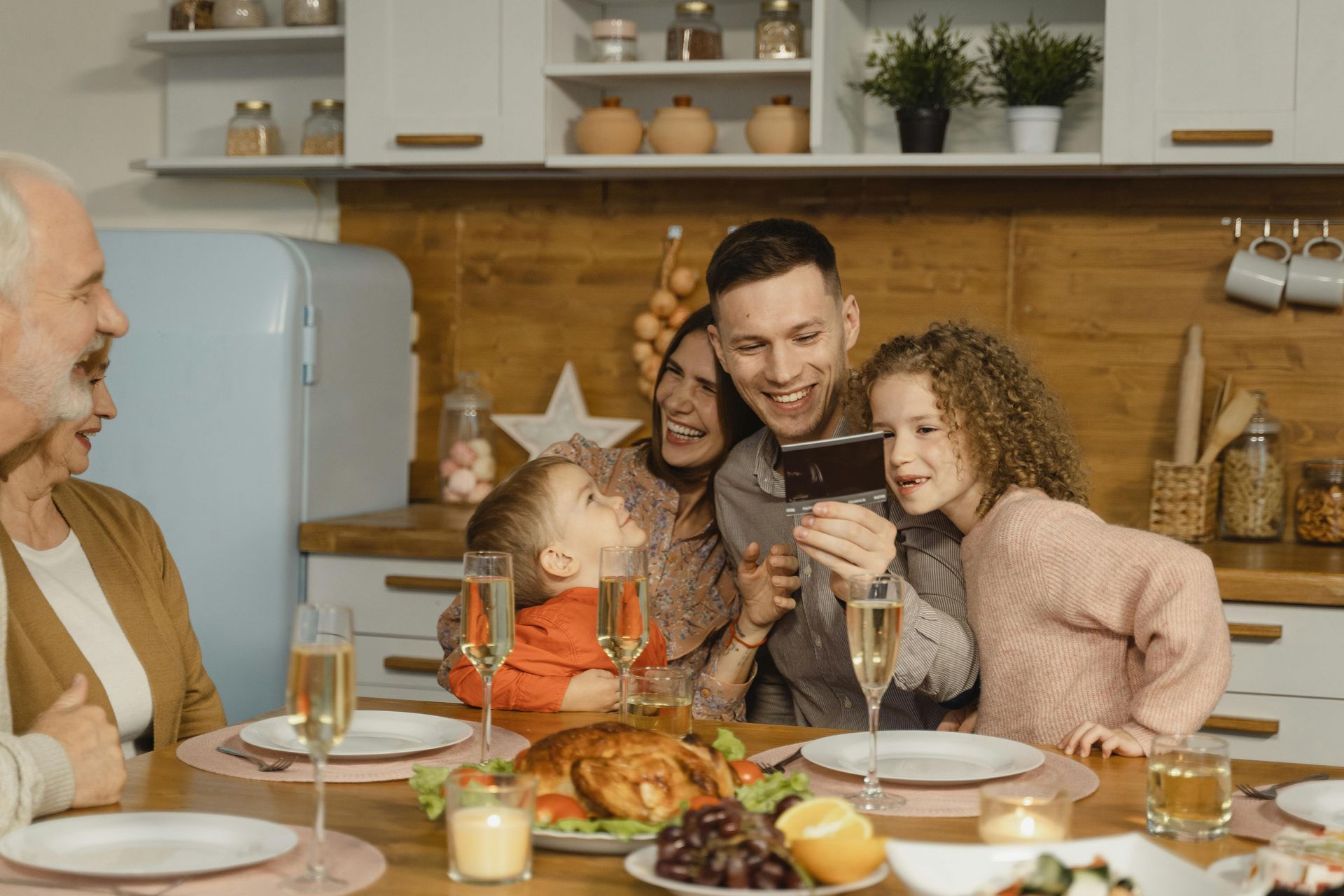A family is sitting at a table taking a selfie with a cell phone.