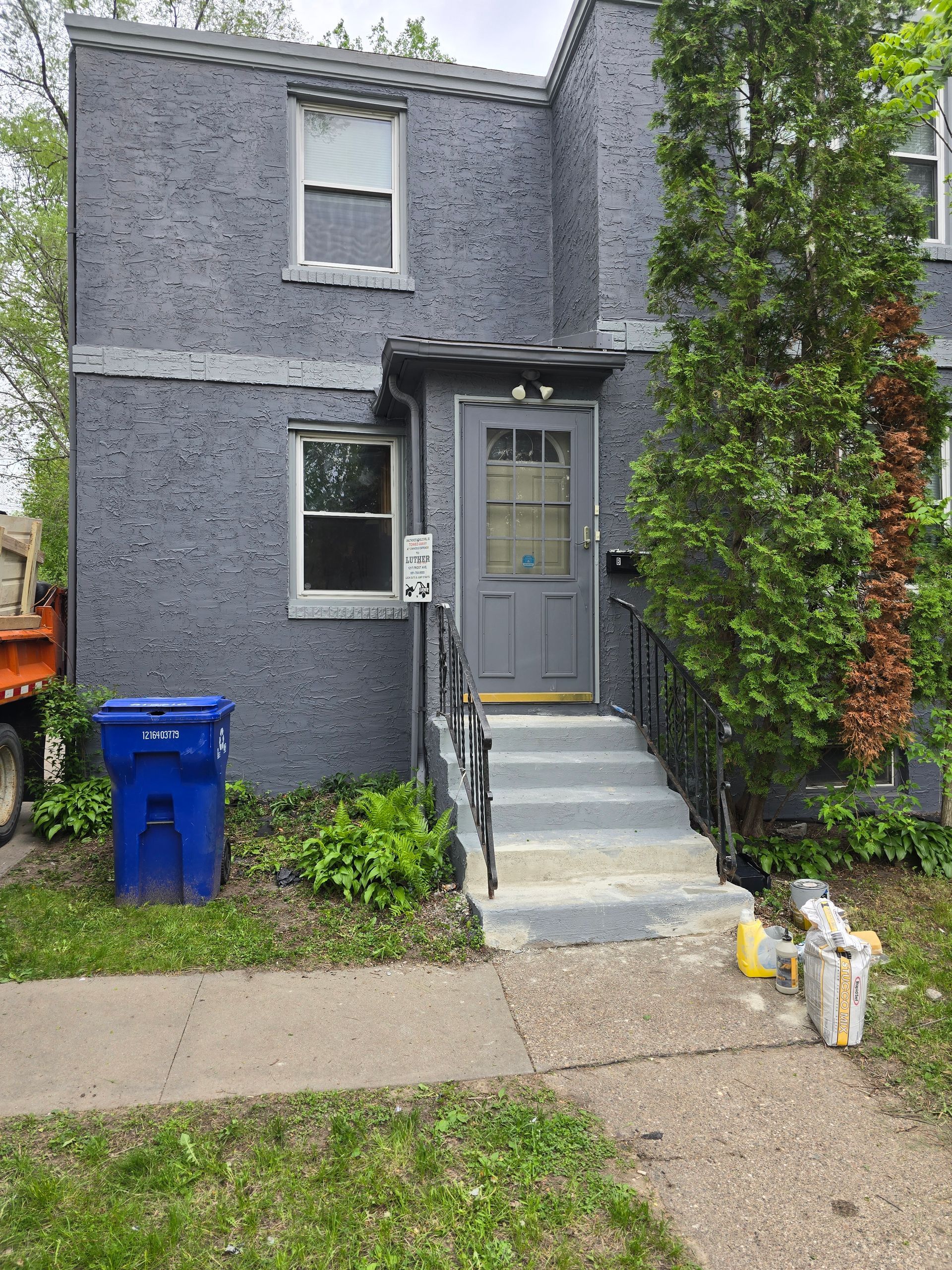 A gray house with a blue trash can in front of it.