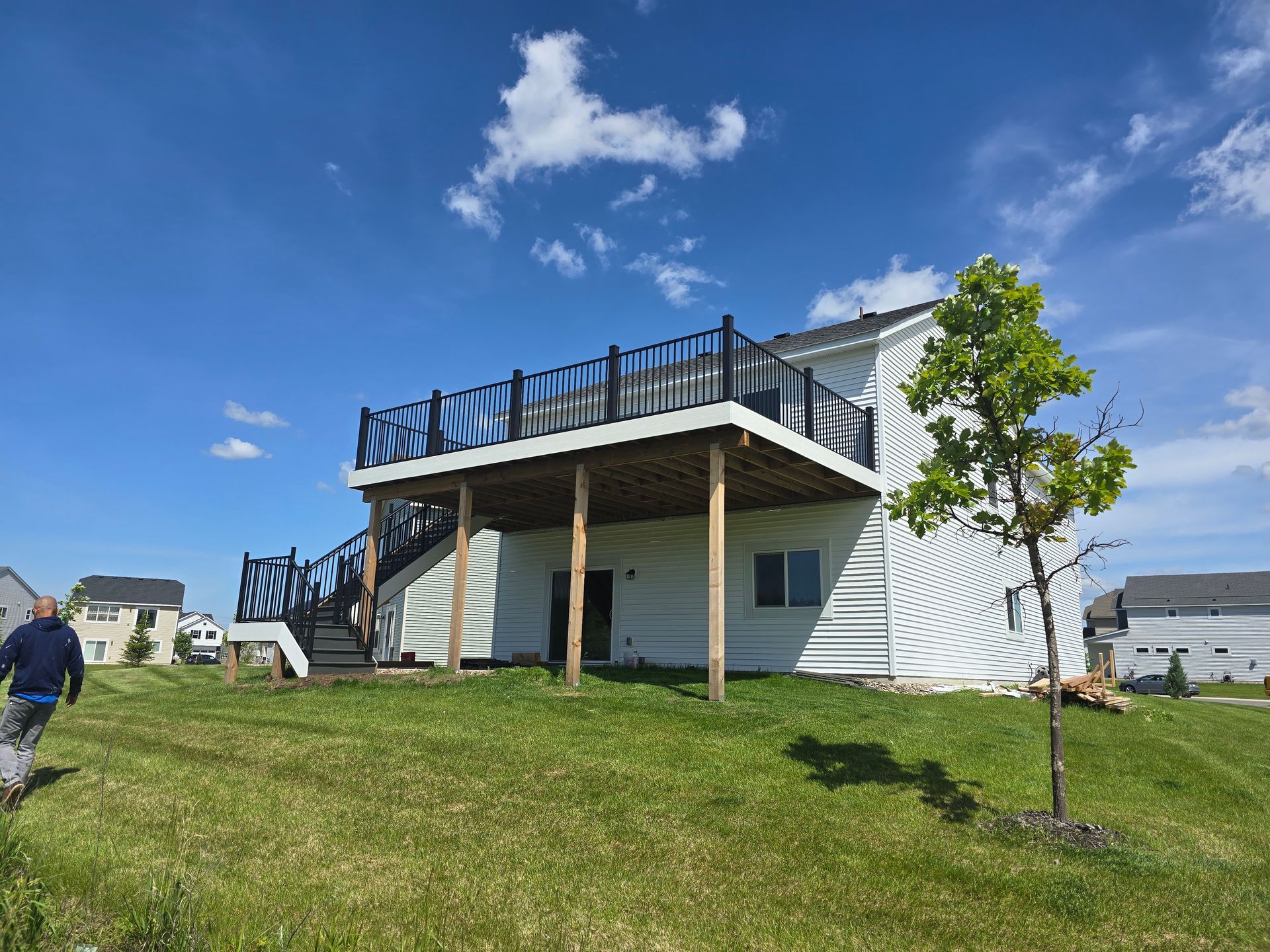 A man is walking in front of a house with a large deck.