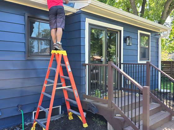 A man is standing on a ladder in front of a blue house.