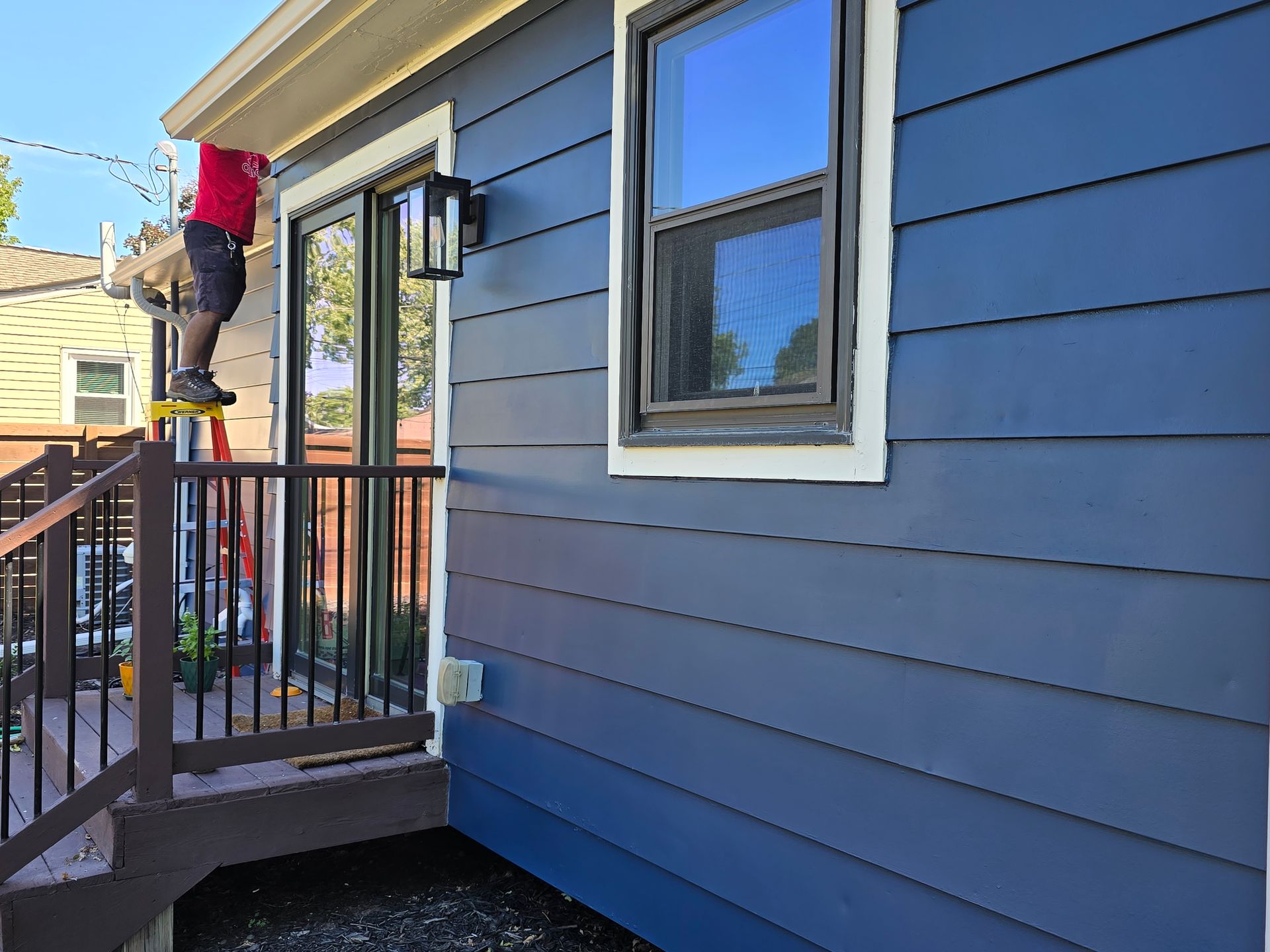 A man is painting the side of a blue house.