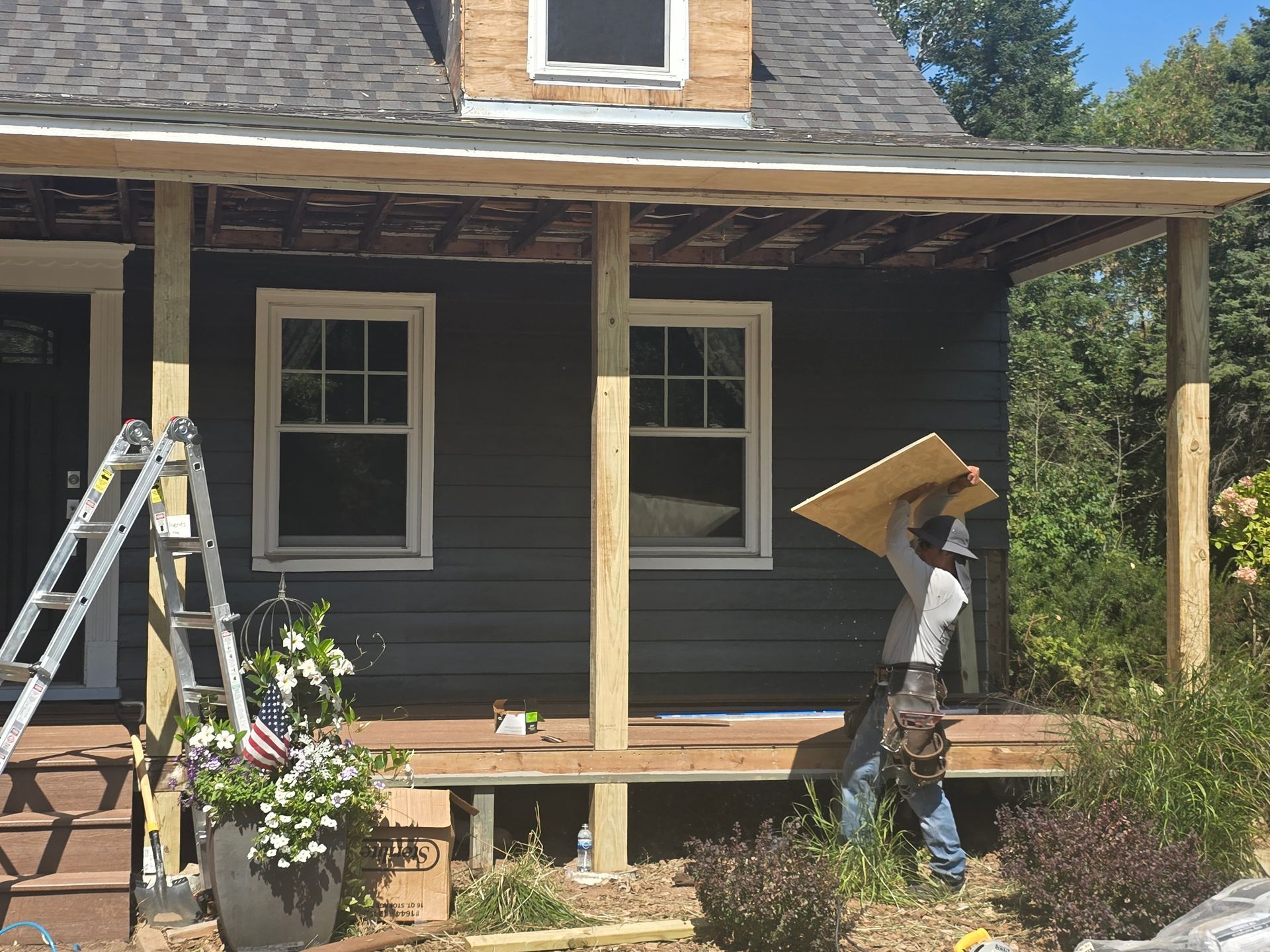 A man is carrying a piece of wood on a porch of a house.