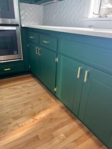 A kitchen with green cabinets and wooden floors.