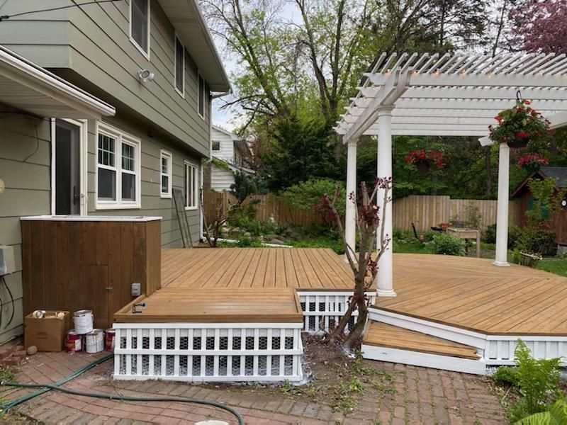 A wooden deck with a pergola and stairs in front of a house.