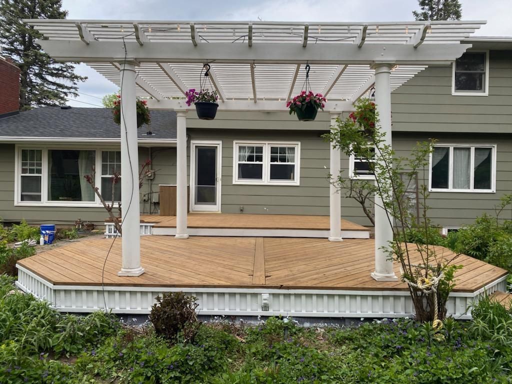 A house with a pergola and a wooden deck in front of it.