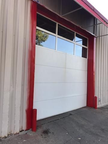 A white garage door with a red trim on the side of a building.