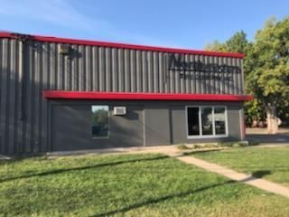 A large gray building with a red roof is sitting on top of a lush green field.