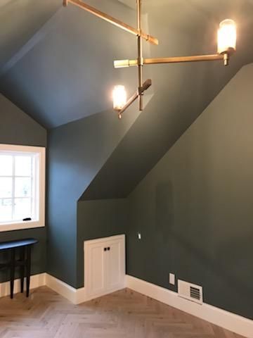 A room with green walls and a window with a chandelier hanging from the ceiling.