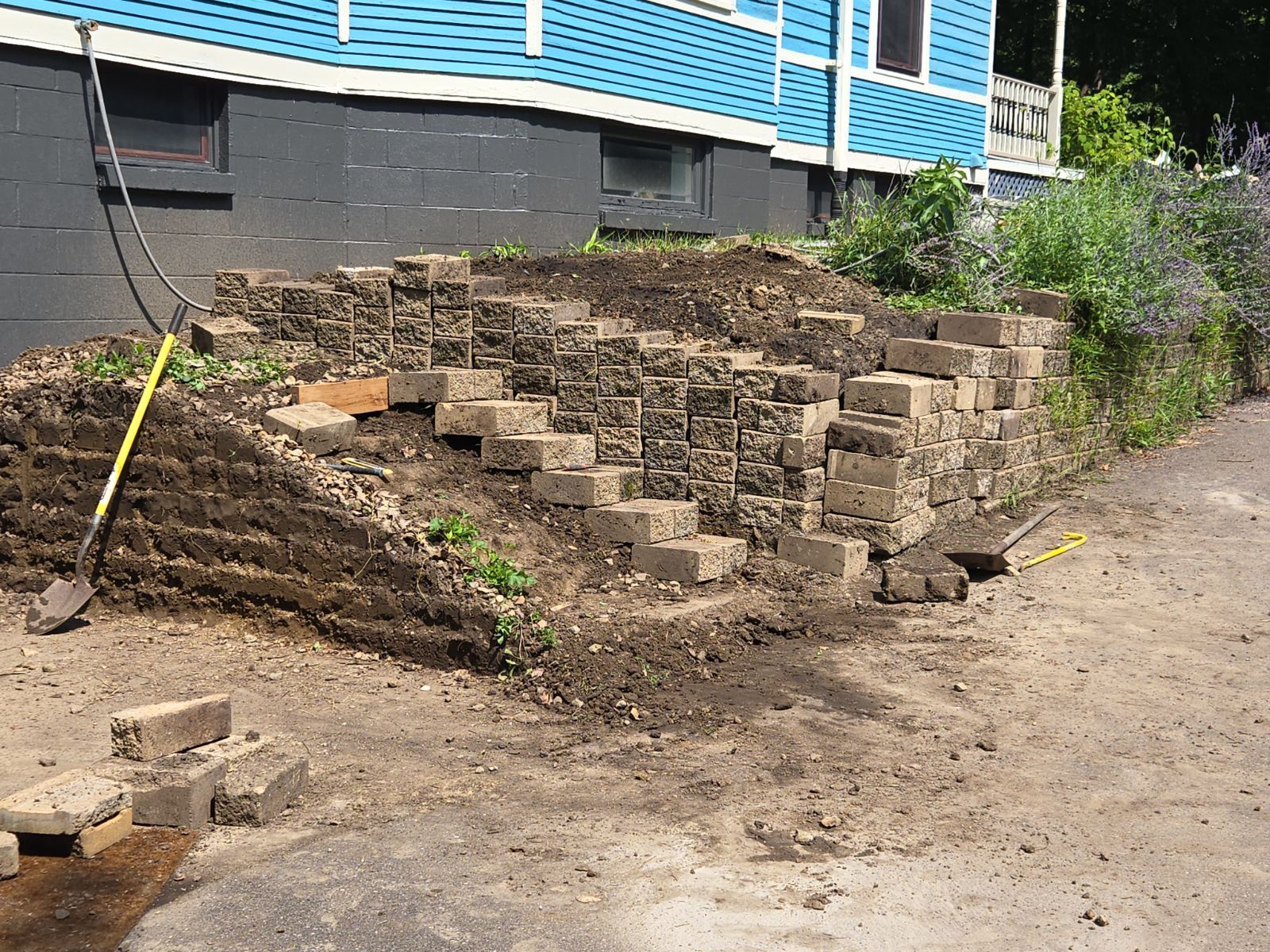 A brick wall is being built in front of a blue house.