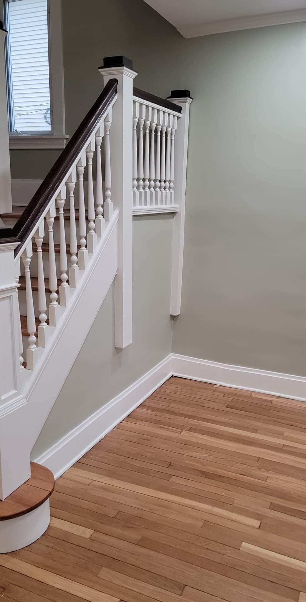 A white staircase with a wooden railing in an empty room with hardwood floors.