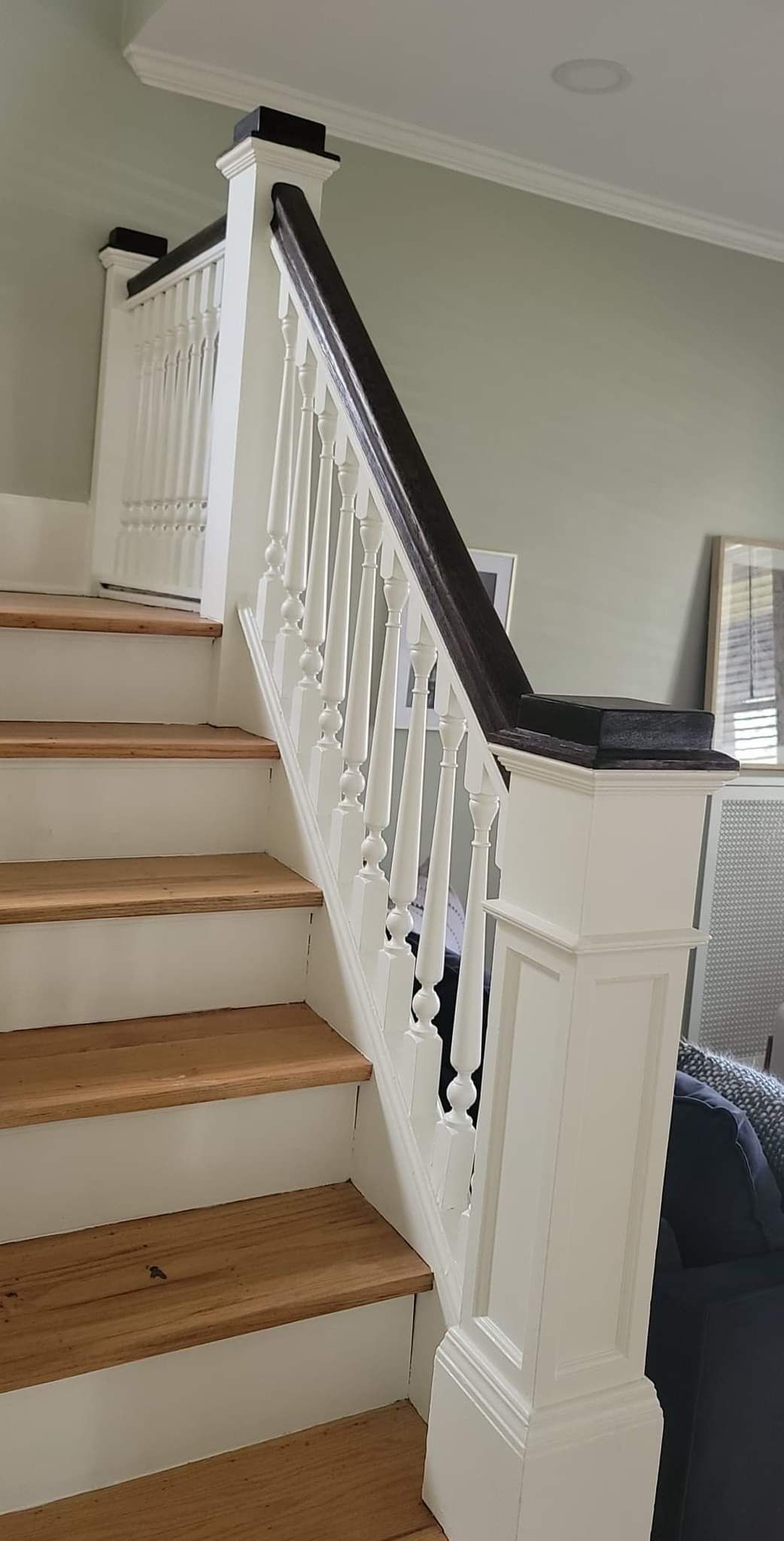 A white staircase with wooden steps and a black railing in a living room.
