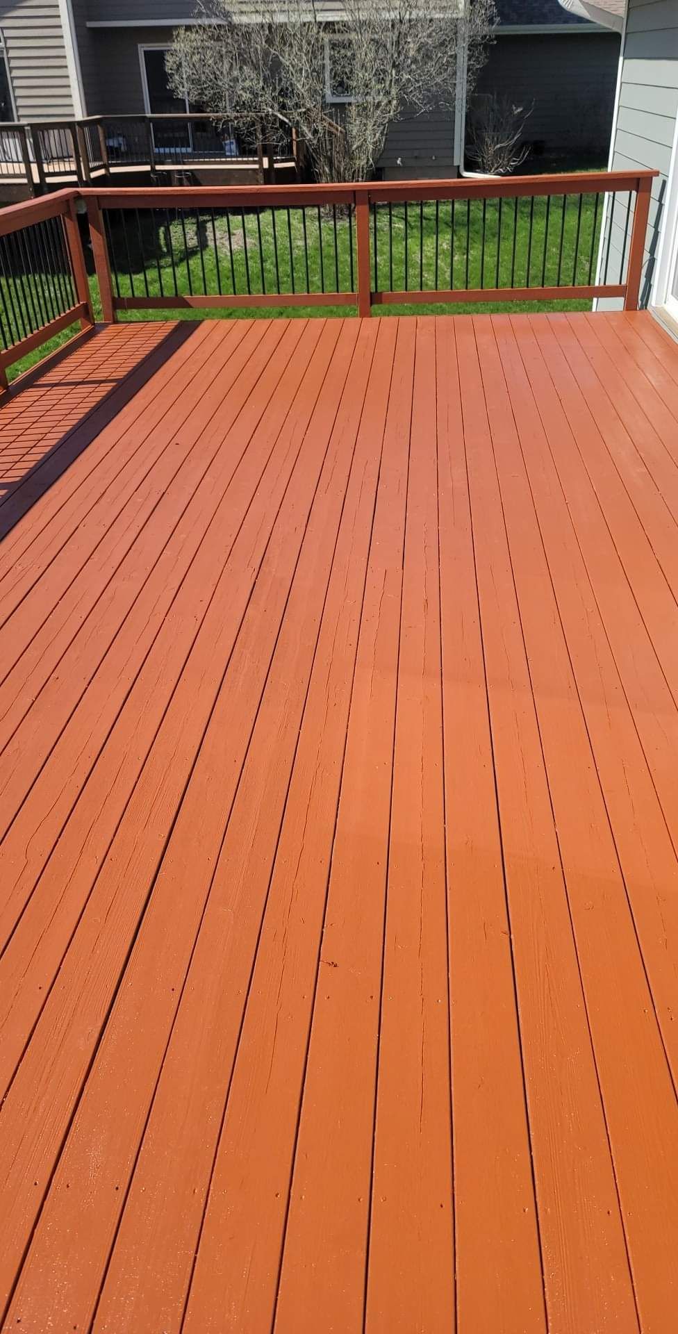 A red wooden deck with a railing and a house in the background.