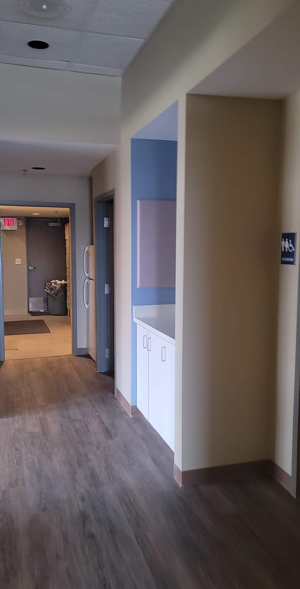 A hallway with hardwood floors and a refrigerator in a building.