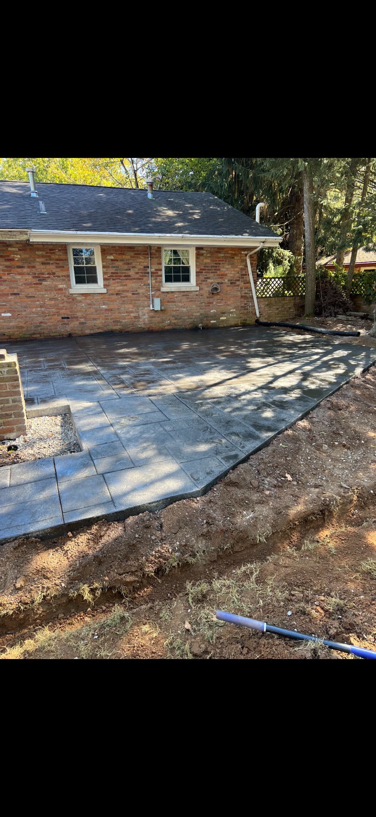 Brick building with concrete patio, surrounded by dirt and trees, sunny day.
