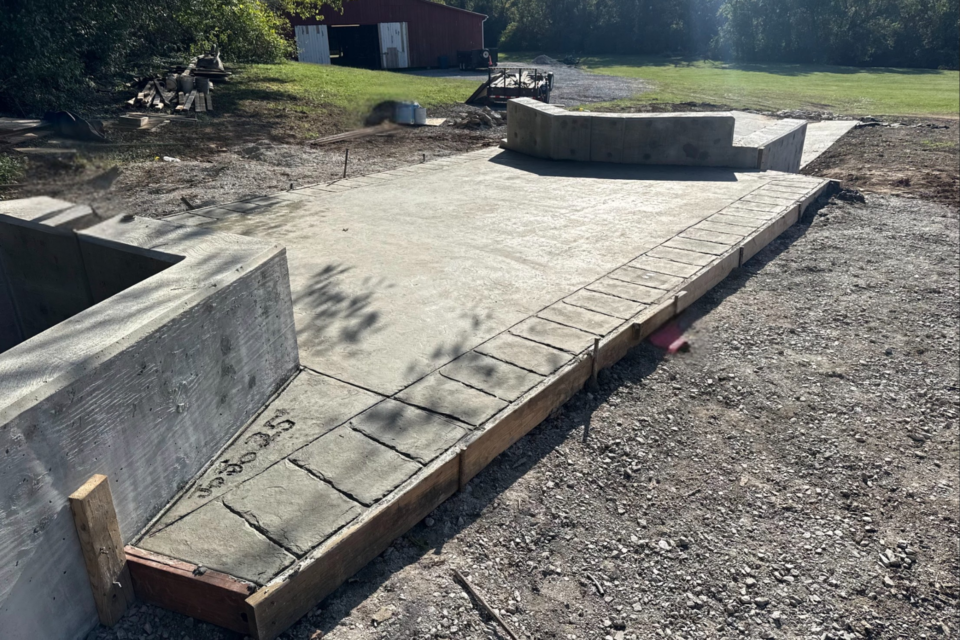 Concrete patio under construction, with wooden borders and cinder block retaining walls. Gravel ground.